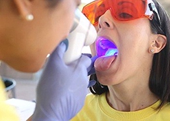 A dental professional examining the inside of a female patient’s mouth using the OralID device