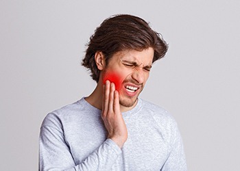 A young male holding his cheek that is radiating red because of intense pain