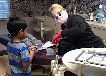 Dentist talking to two kids in dental exam chair