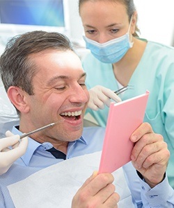 Older man in dental chair looking at his smile in the mirror