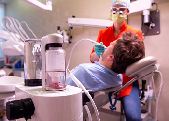 A dentist using an air abrasion stain removal device on a male patient’s smile