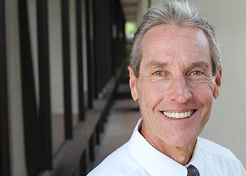 An older gentleman wearing a white button-down shirt and tie smiling after receiving his dentures