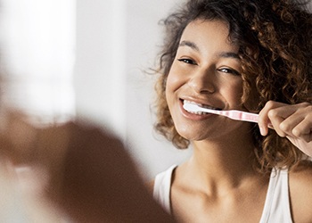 A young woman brushing her teeth while standing in her bathroom