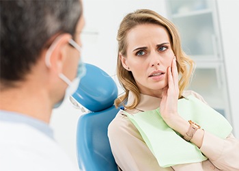 Woman in dental chair holding cheek