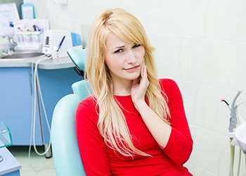 A young woman with blonde hair holds her cheek in pain in preparation for a tooth extraction