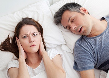 Woman covering ears next to snoring man