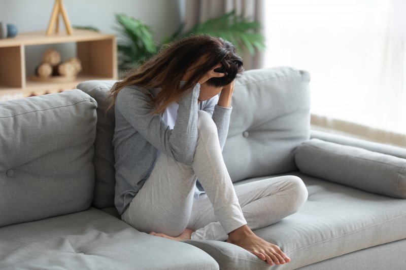 a woman sitting on a couch with her head in her hands and experience anxious feelings